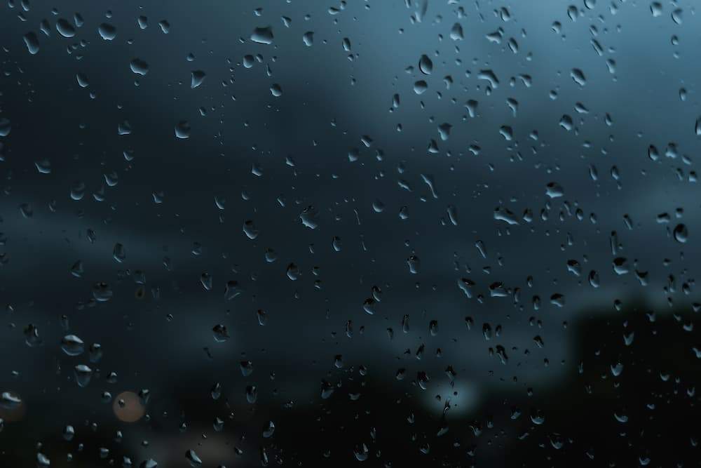 Dark window glass covered in raindrops during a storm, illustrating the required cleaning and frame maintenance of hurricane windows or impact windows after severe weather.